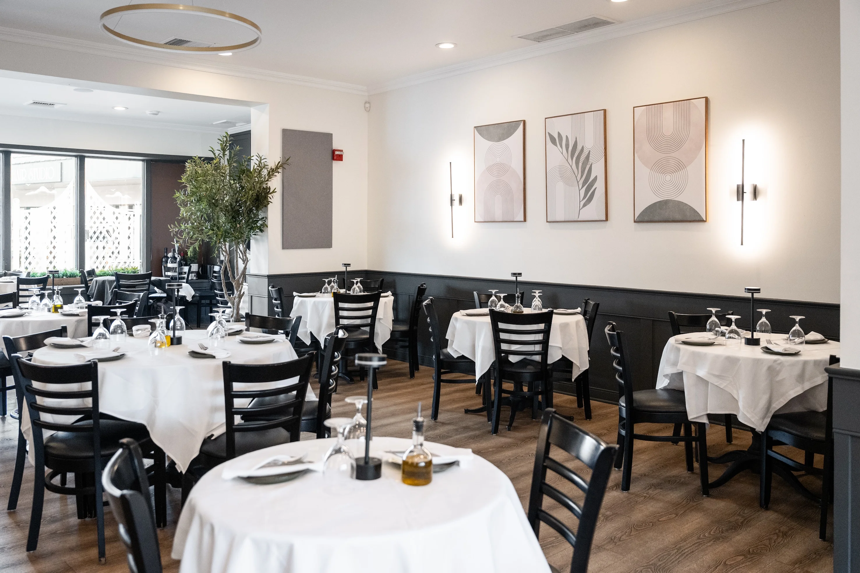 Private dining setup at Toscana on Main Eastchester featuring white tablecloths, black chairs, and modern artwork on the walls, creating a welcoming atmosphere
