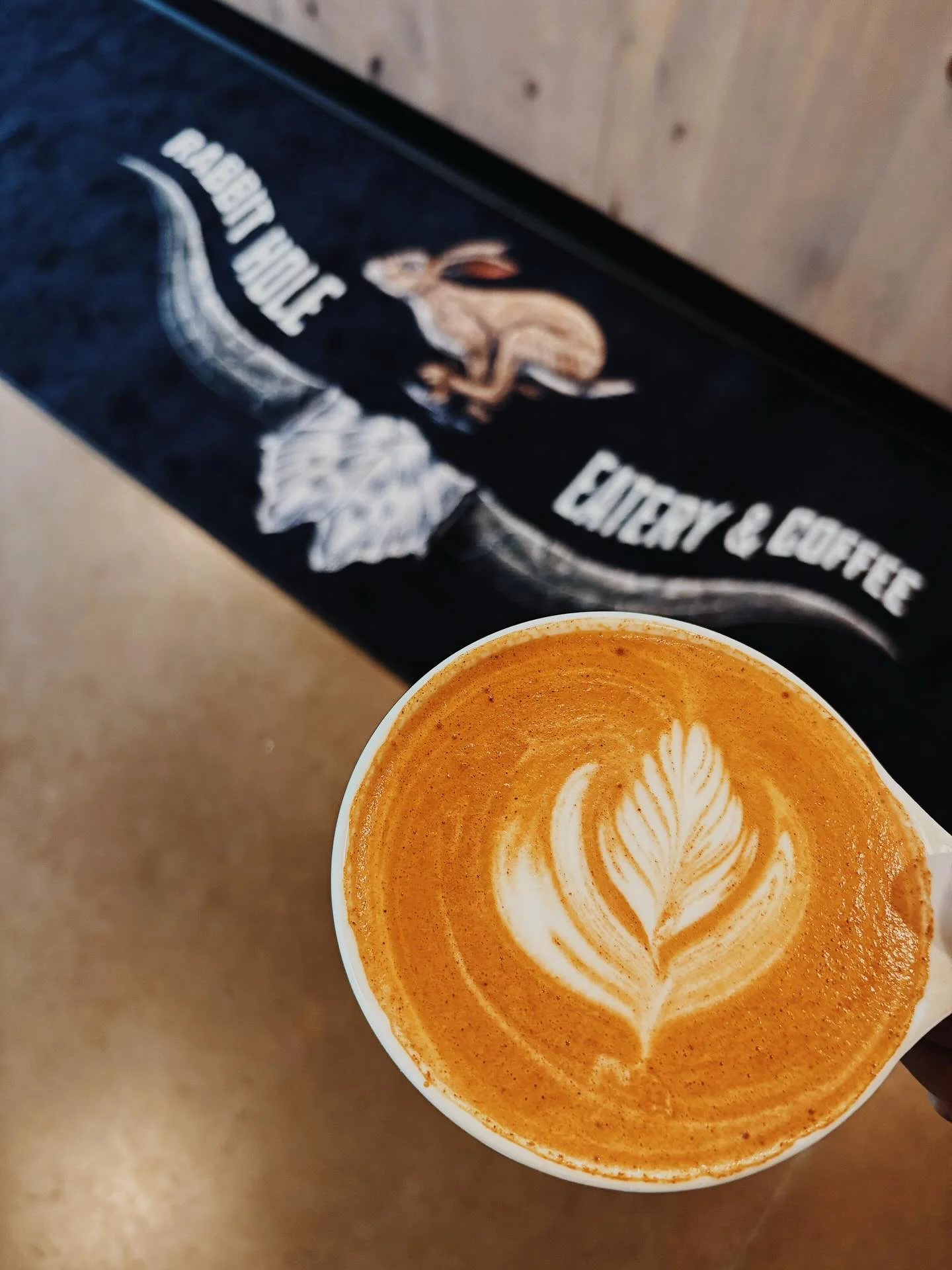 Rabbit Hole Eatery craft latte with logo in background.