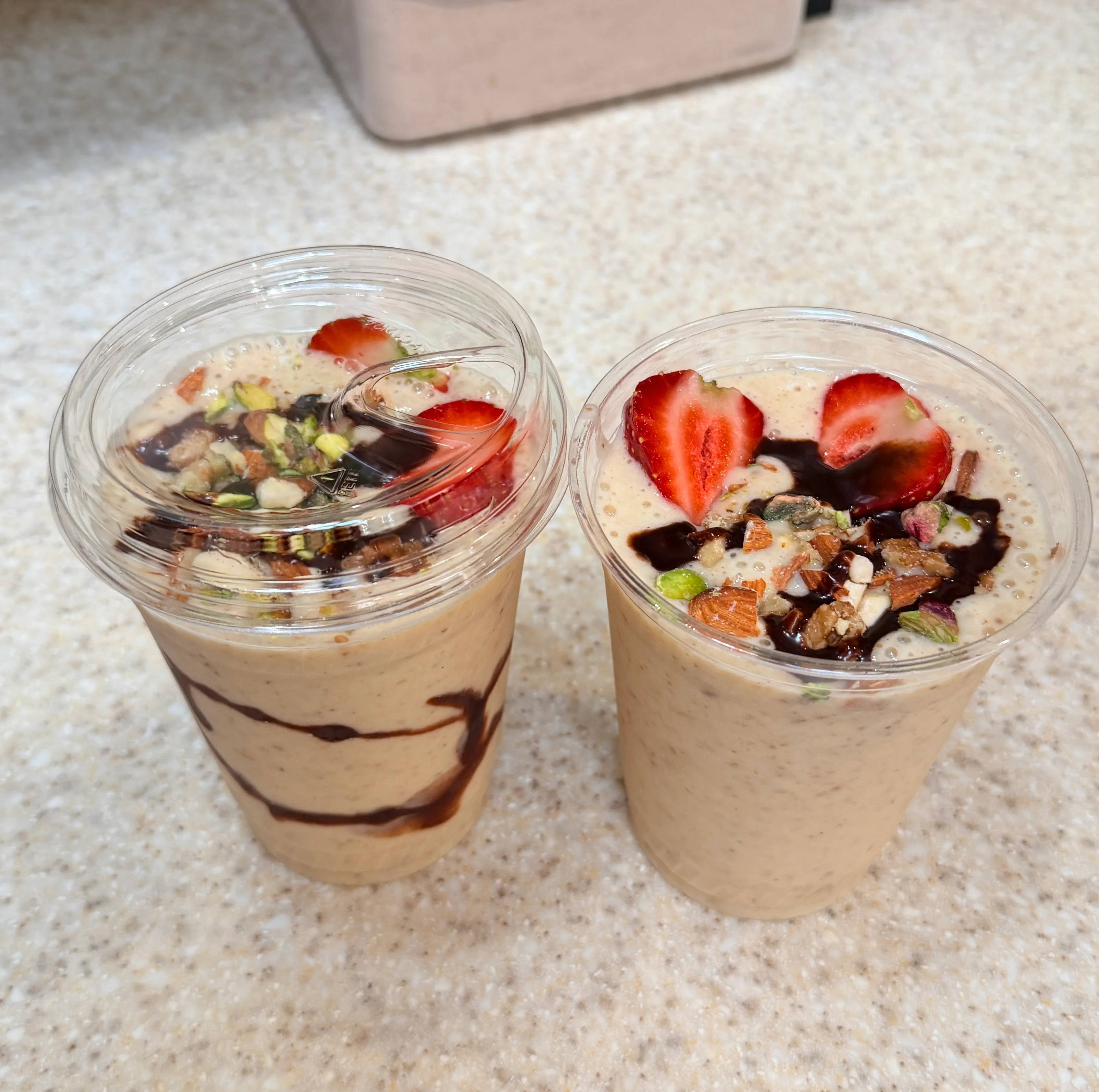 Two smoothies topped with strawberries and nuts in clear cups.
