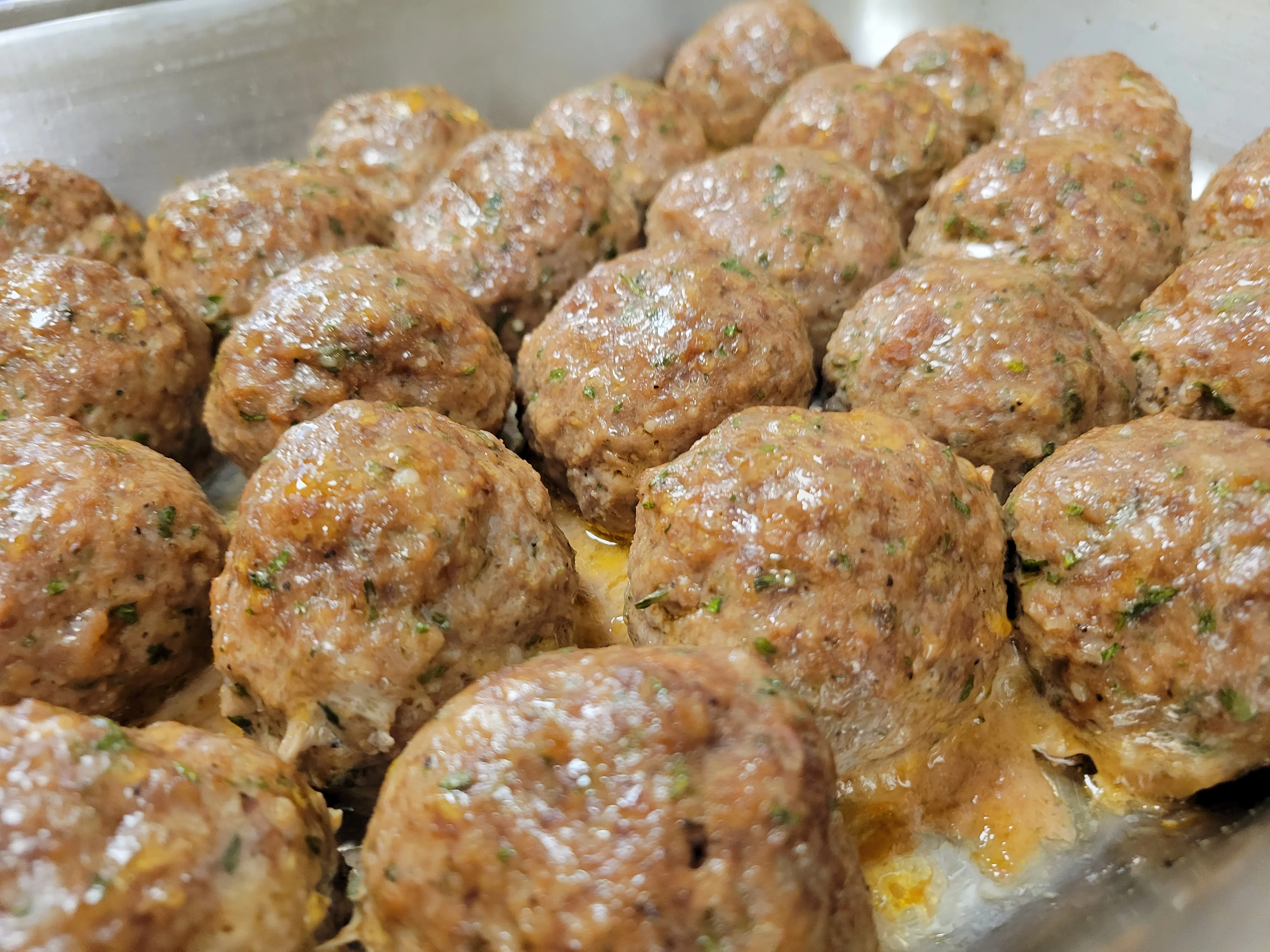 A tray filled with freshly cooked meatballs, arranged closely together and glistening with seasoning.