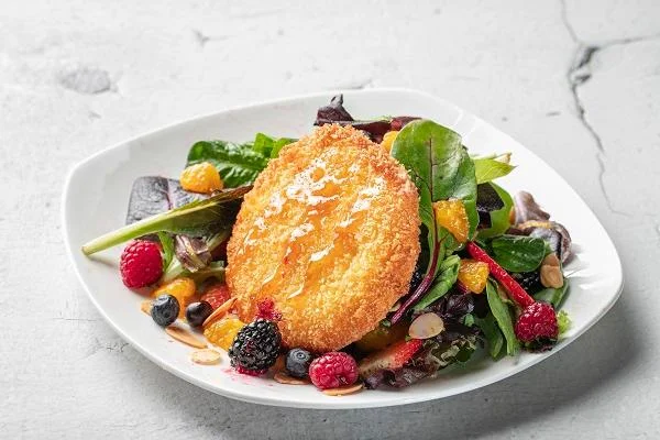 A colorful salad featuring mixed greens, berries, and a crispy golden round item, arranged on a white plate.
