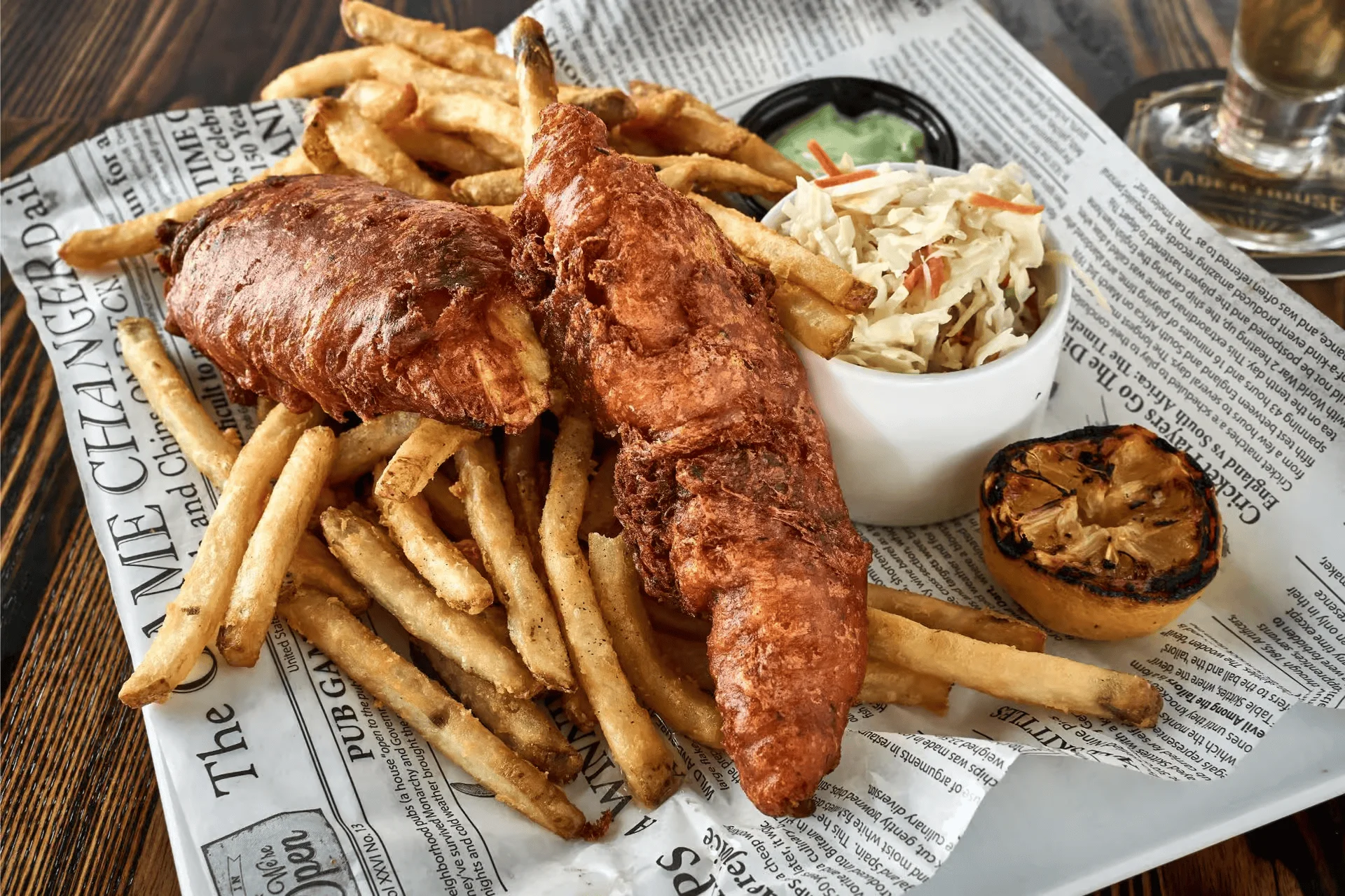 A plate of crispy fried fish fillets served alongside golden French fries and coleslaw, with a grilled lemon for garnish.
