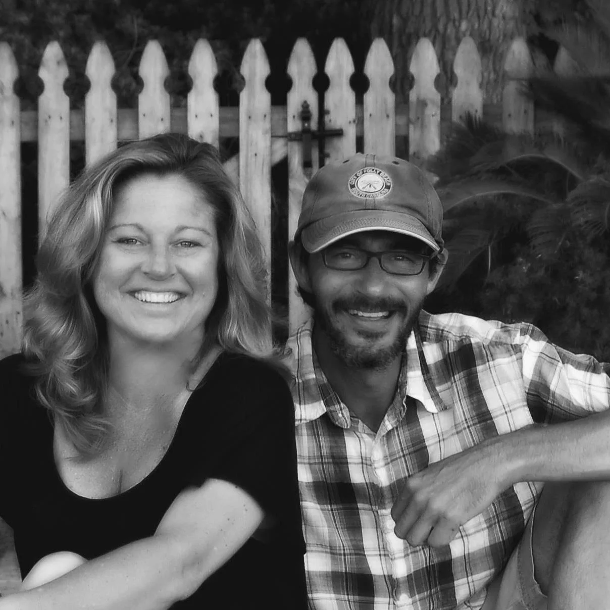 Two smiling individuals sitting outdoors in black and white