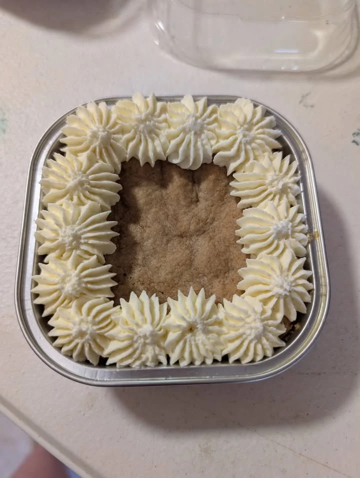 A square baking dish filled with a cookie topped with white frosting in a decorative pattern.