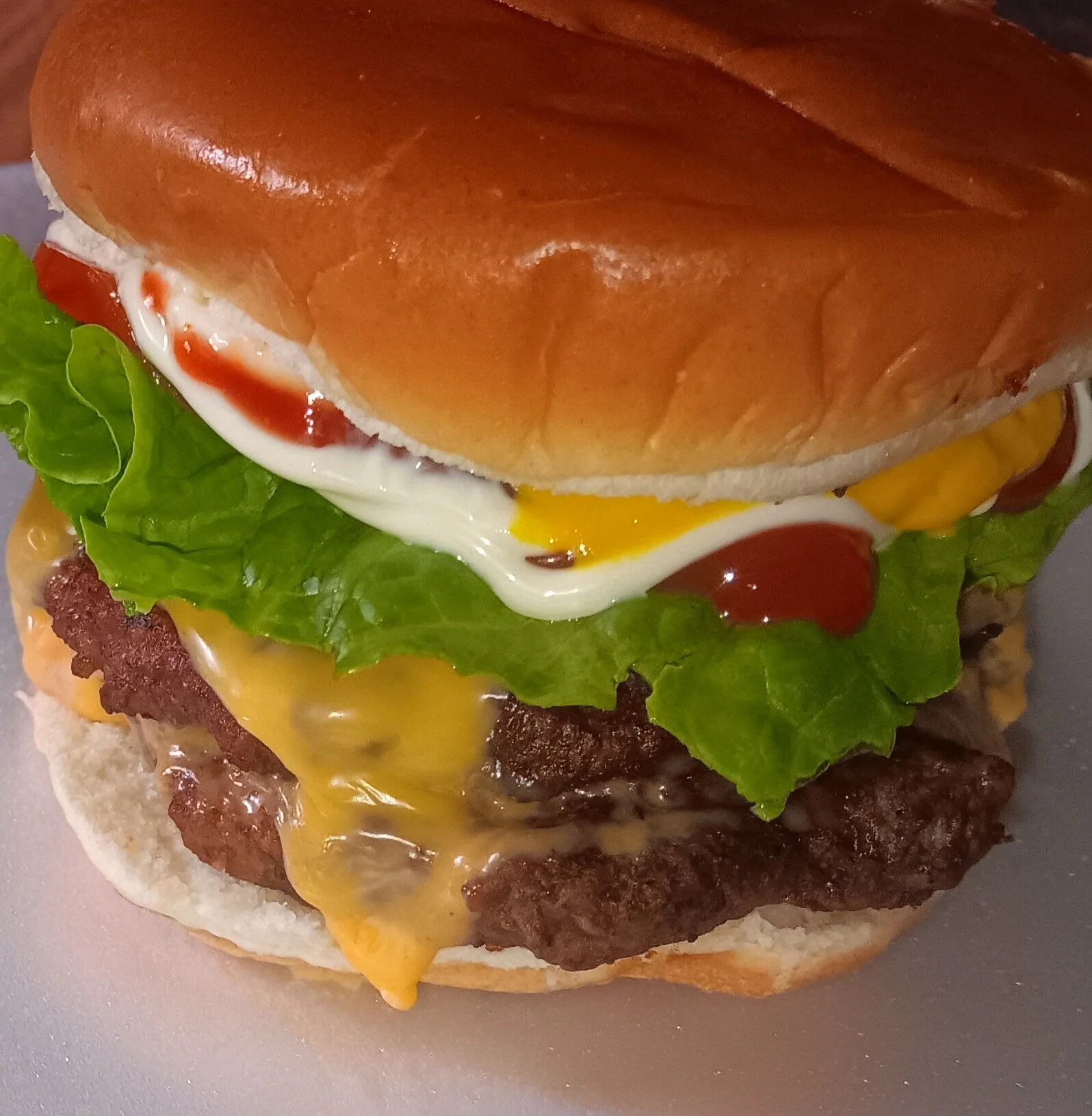 A close-up of a stacked hamburger with lettuce, cheese, ketchup, mustard, and mayonnaise, all in a toasted bun.