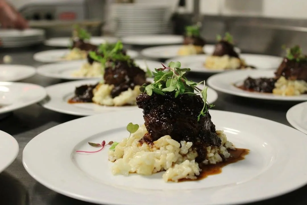 A gourmet dish featuring tender meat served on a bed of creamy risotto, garnished with fresh microgreens. The presentation is elegant, with a rich sauce enhancing the flavors.