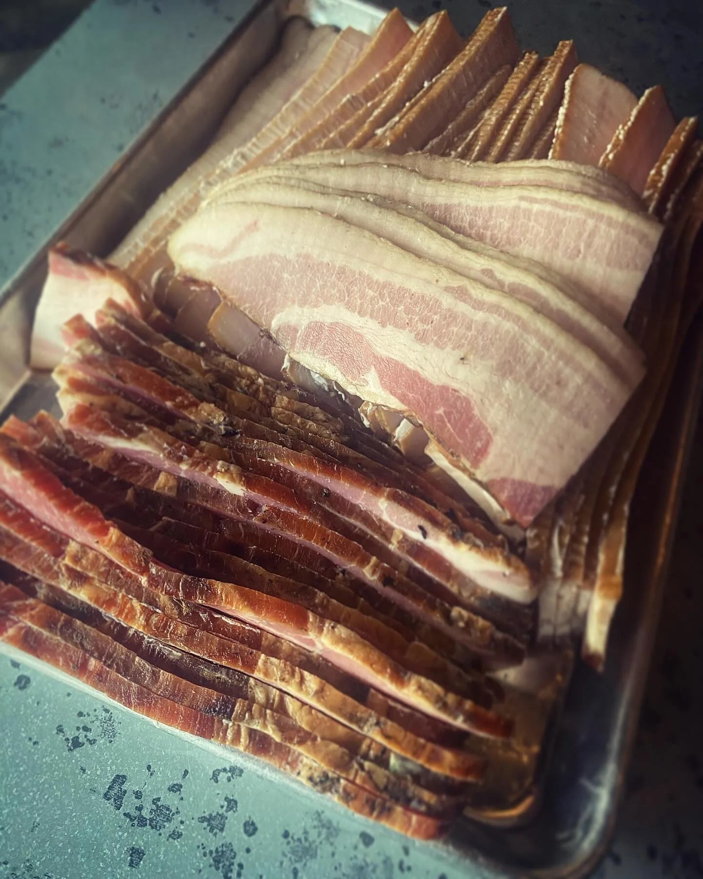 A tray filled with different types of bacon, layered and ready for use.