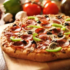 A delicious pizza topped with pepperoni, olives, green peppers, onions, and mushrooms, sitting on a wooden board with vegetables in the background.