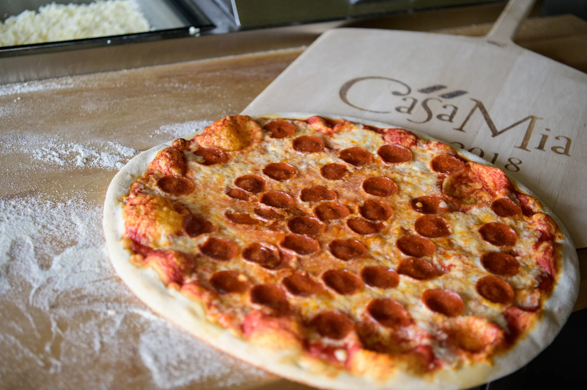 A freshly made pepperoni pizza placed on a wooden pizza peel, with flour scattered on the surface.
