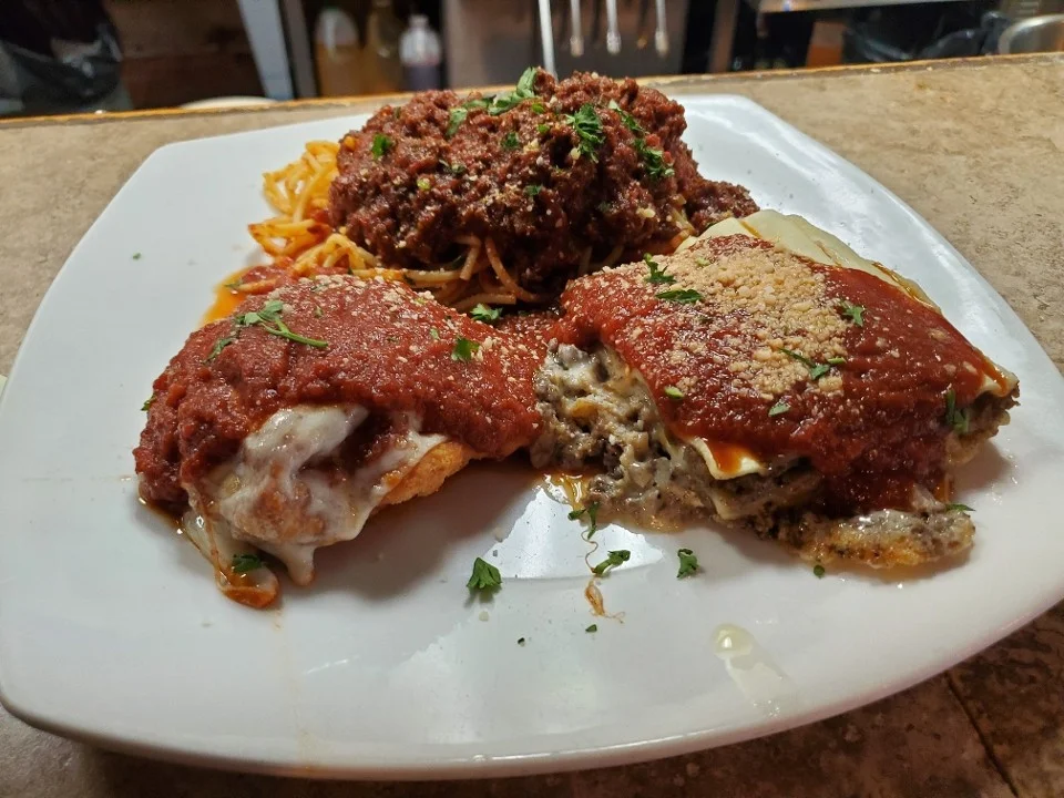 Italian lasagna and spaghetti with meat sauce on a white plate