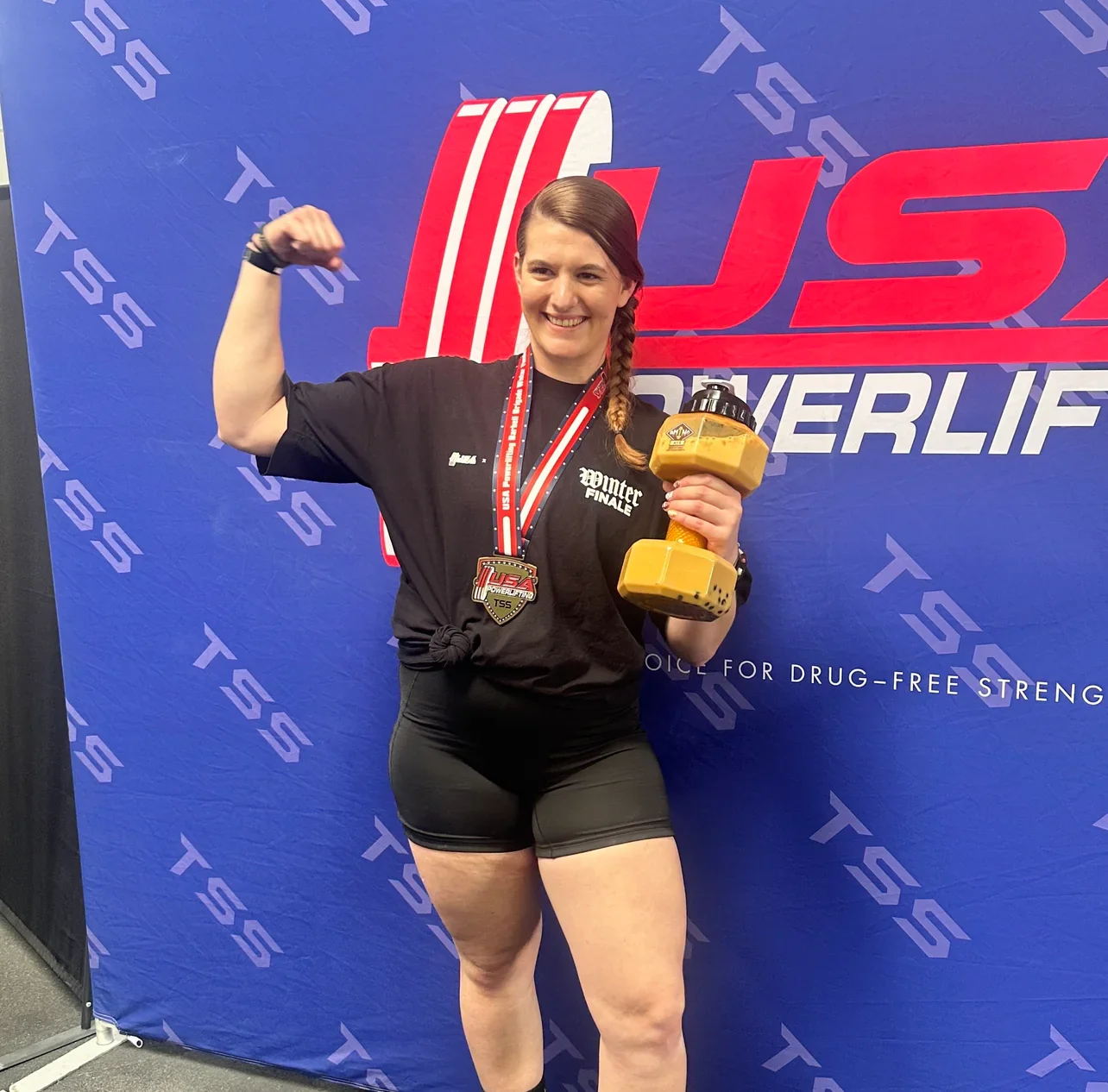 Athlete celebrating with trophy and dumbbell at powerlifting event