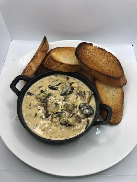 A bowl of creamy mushroom sauce served with toasted bread slices on a white plate, garnished with parsley.