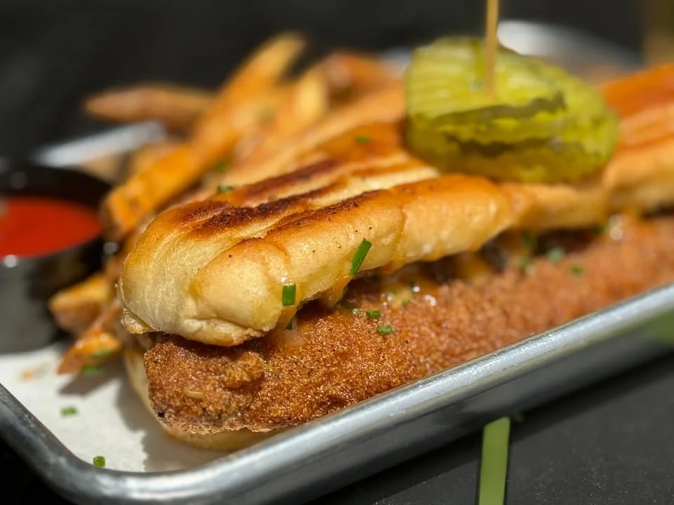 A delicious dish featuring grilled fish on a bed of crispy bread, accompanied by fries and pickles, with a side of dipping sauce.