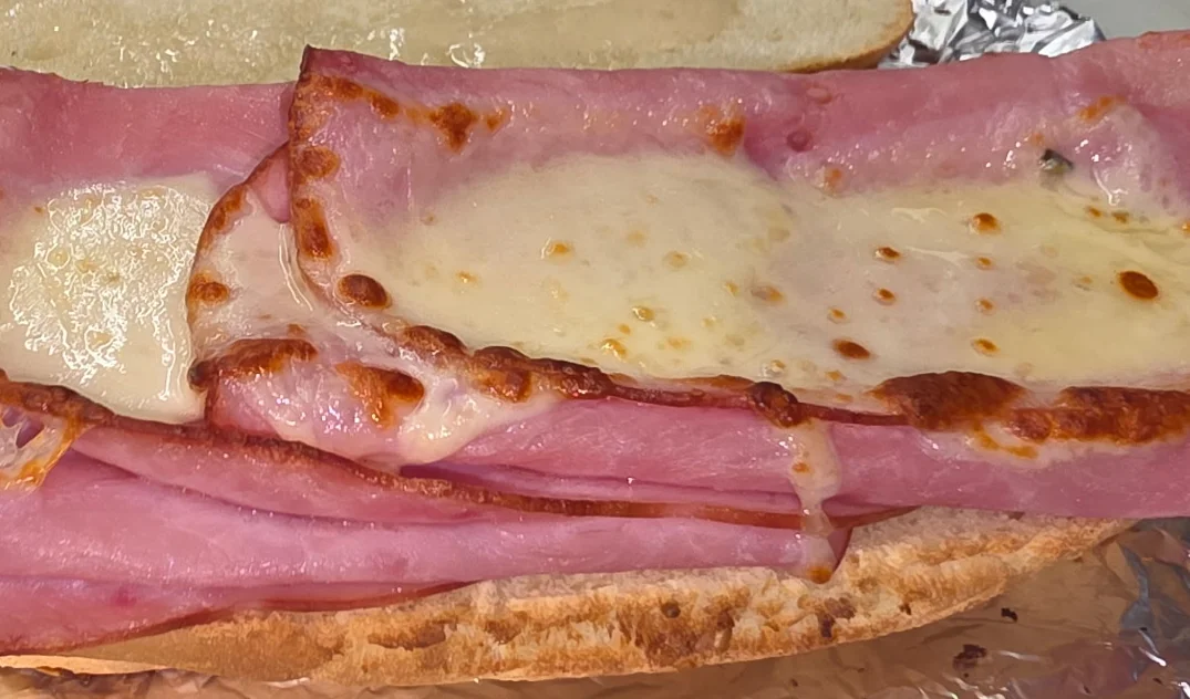 A sandwich made with ham and melted cheese on a hoagie roll, wrapped in foil.
