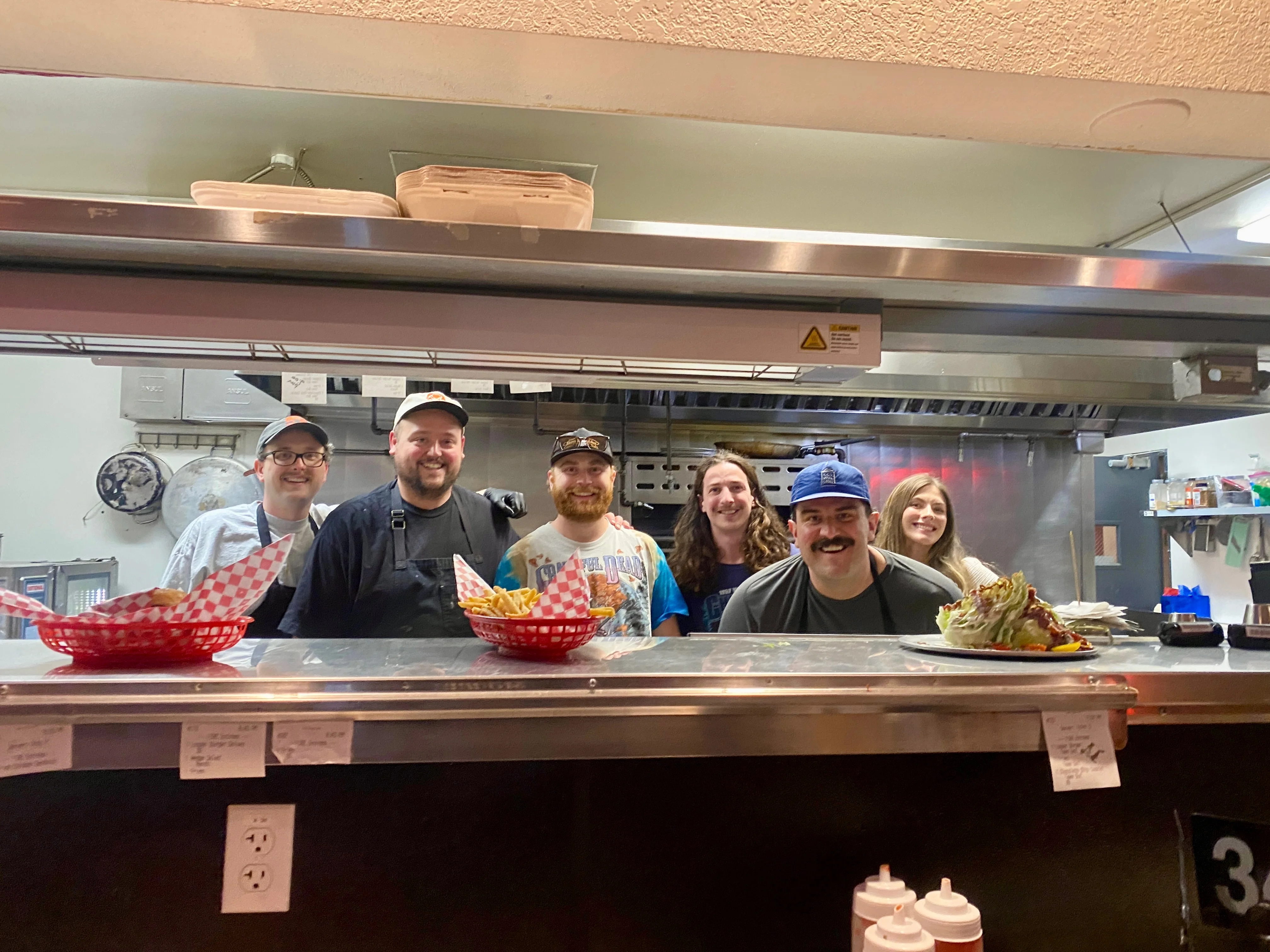 Staff members smiling behind a counter in a restaurant kitchen.