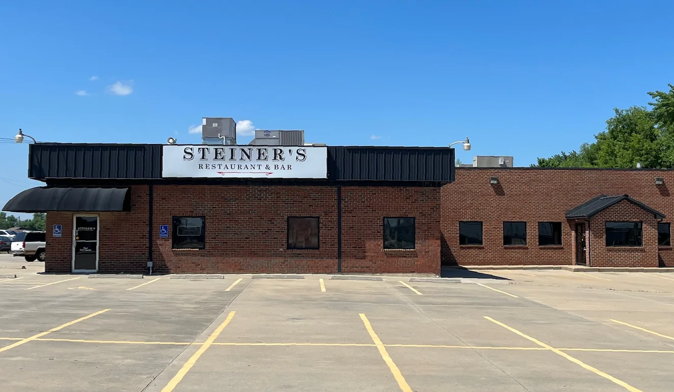 The exterior of a restaurant named Steiner's, featuring a brick facade and parking area under a clear blue sky.