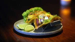 Three vibrant tacos served with lime wedges