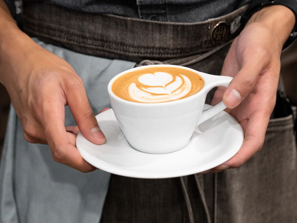 Barista presenting a beautifully crafted latte art in a white cup