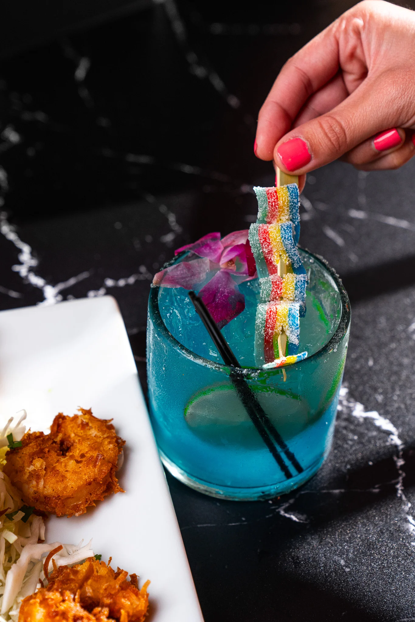 Colorful cocktail with gummy candy garnish and fried shrimp on a plate