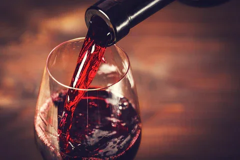 Three bottles of wine with black labels featuring artwork and text. They are arranged on a wooden table with a blurred background of shelves filled with more products.