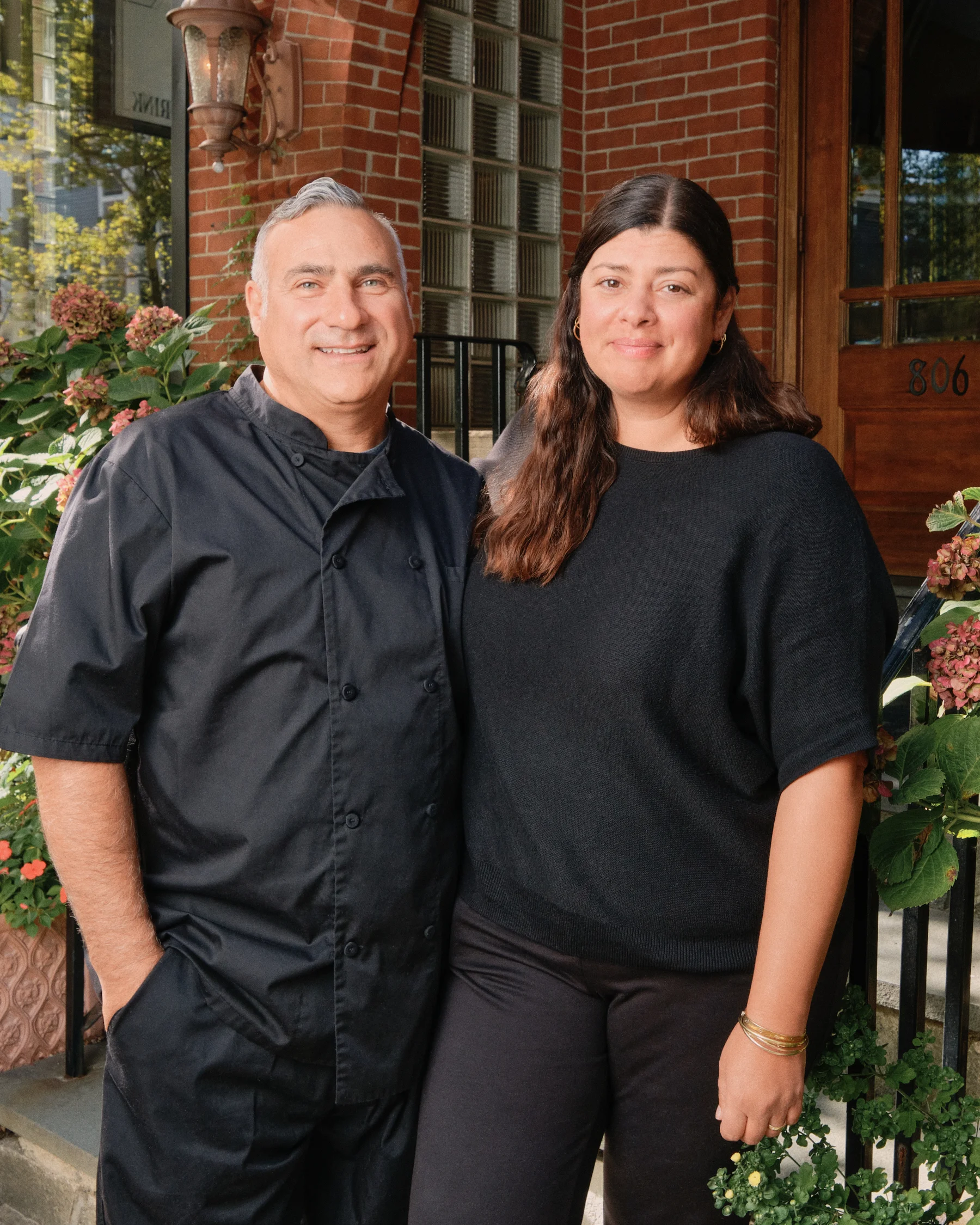 Two restaurant owners smiling outside their establishment.