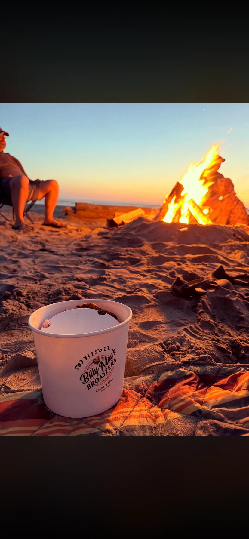 Beach bonfire with a bucket of fried chicken at sunset