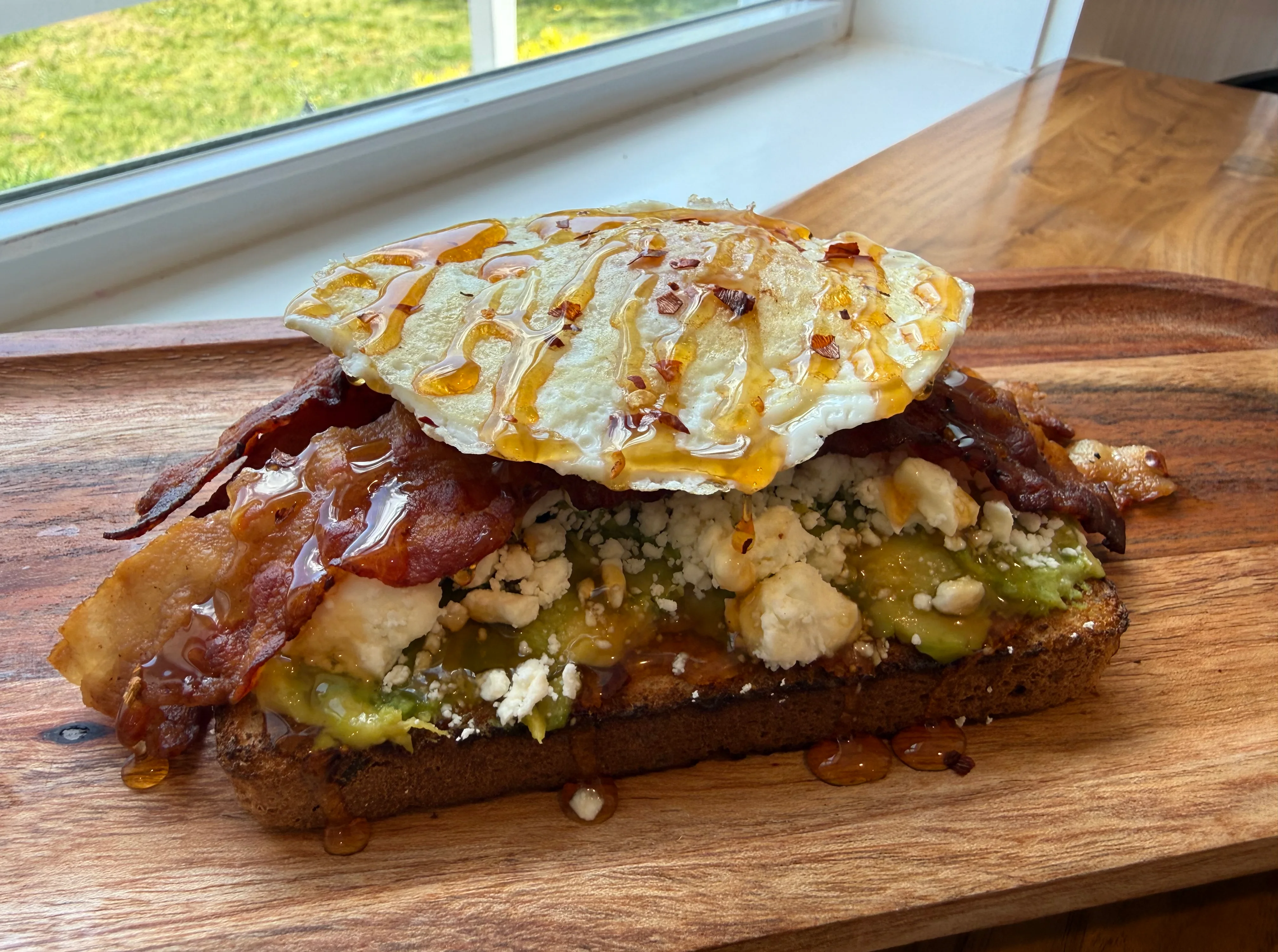 A hearty breakfast sandwich with bacon, egg, and toppings on dark bread.
