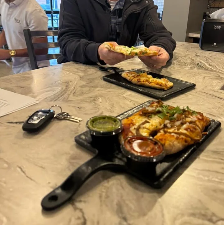 A table setting with a person holding a piece of flatbread, accompanied by plates of food and dipping sauces.