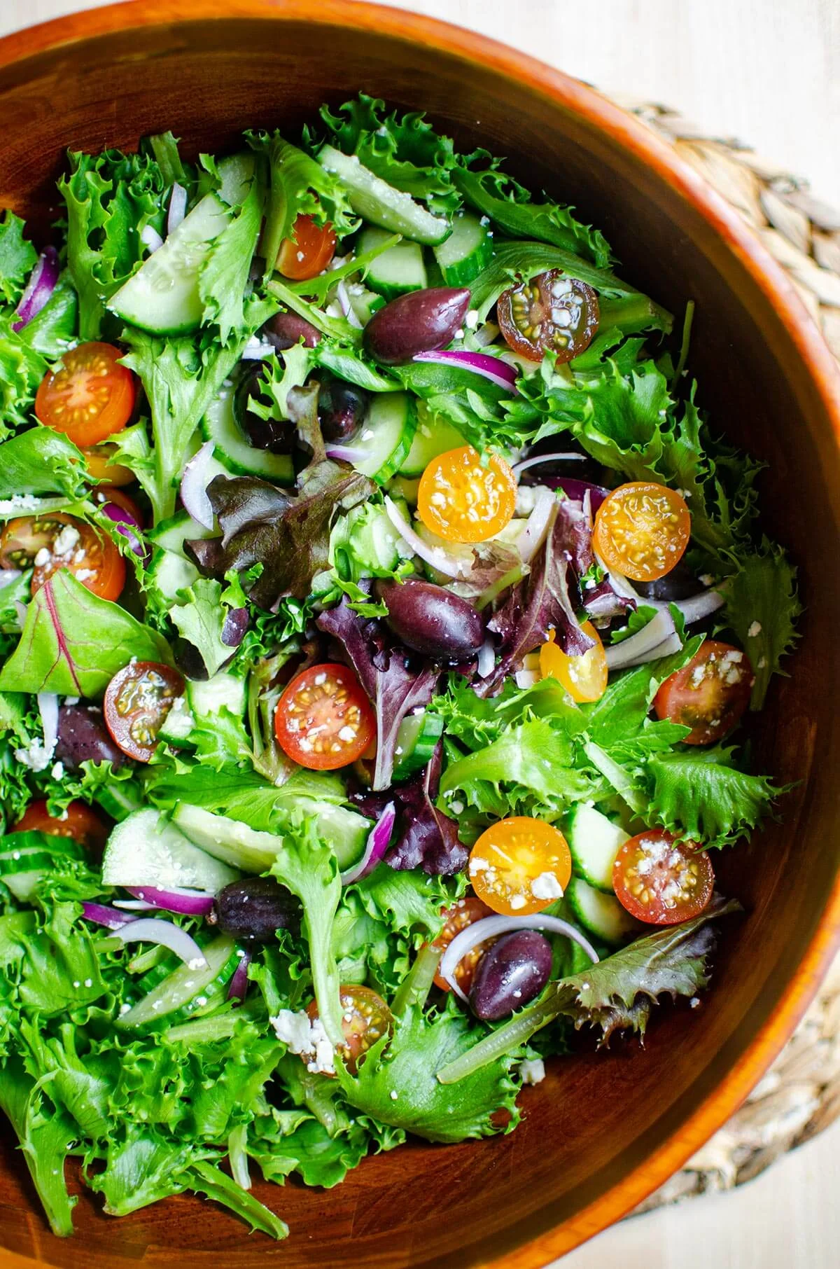 A vibrant salad with mixed greens, tomatoes, cucumber, and black olives in a wooden bowl.