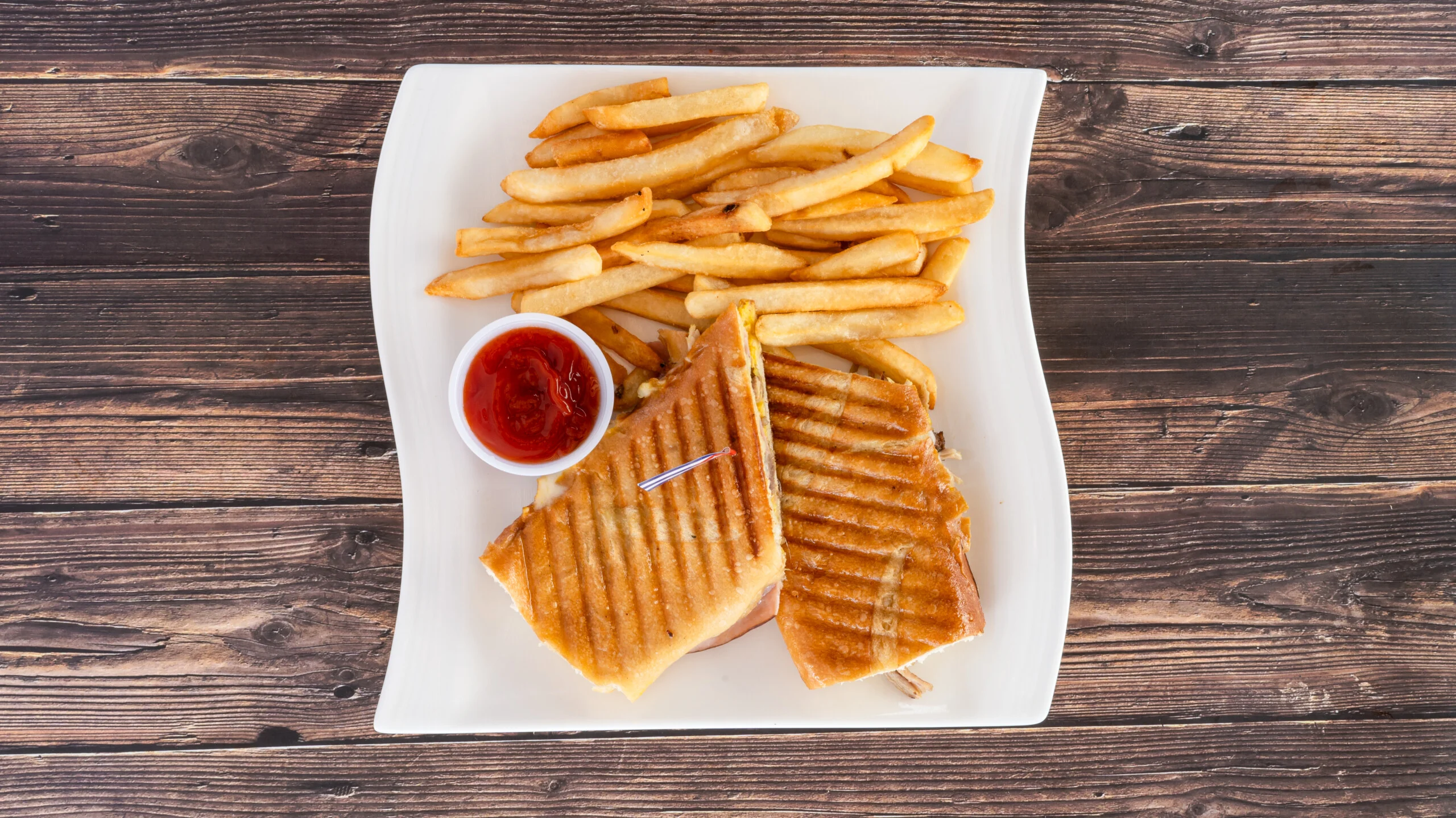 Ta Rica pressed Cuban sandwich with fries and ketchup on a white plate