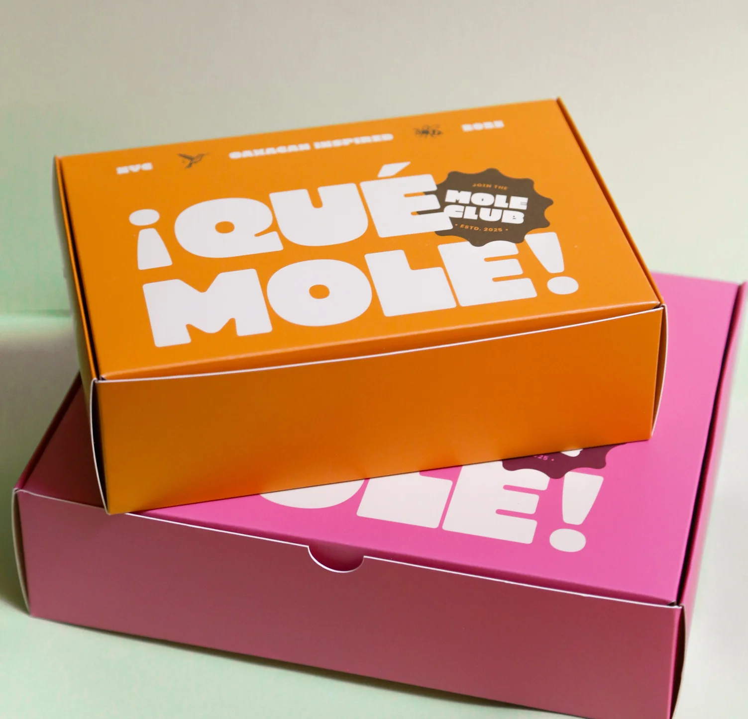Brightly colored ¡Qué Mole! takeout boxes stacked together, showcasing the bold, playful packaging.