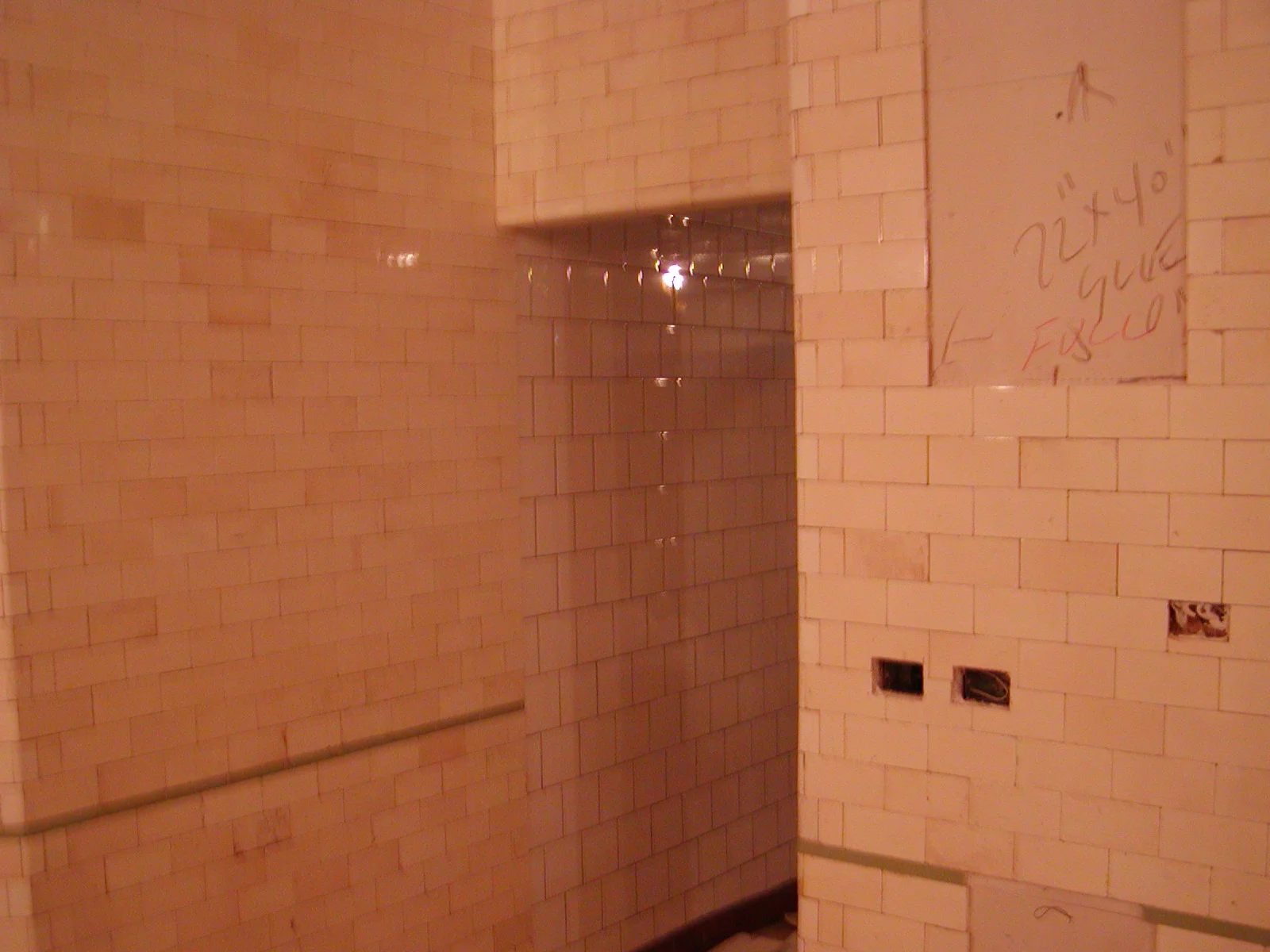 Under construction bathroom with white tiled walls and exposed plumbing