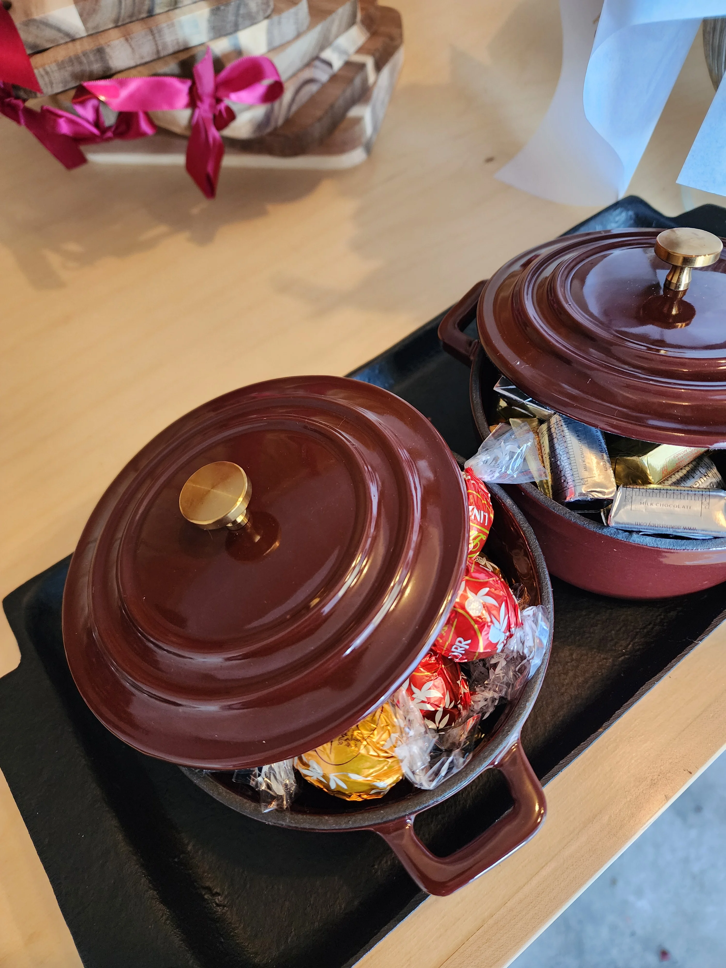 Close-up of two small cooking pots filled with assorted candies, placed on a black serving tray.