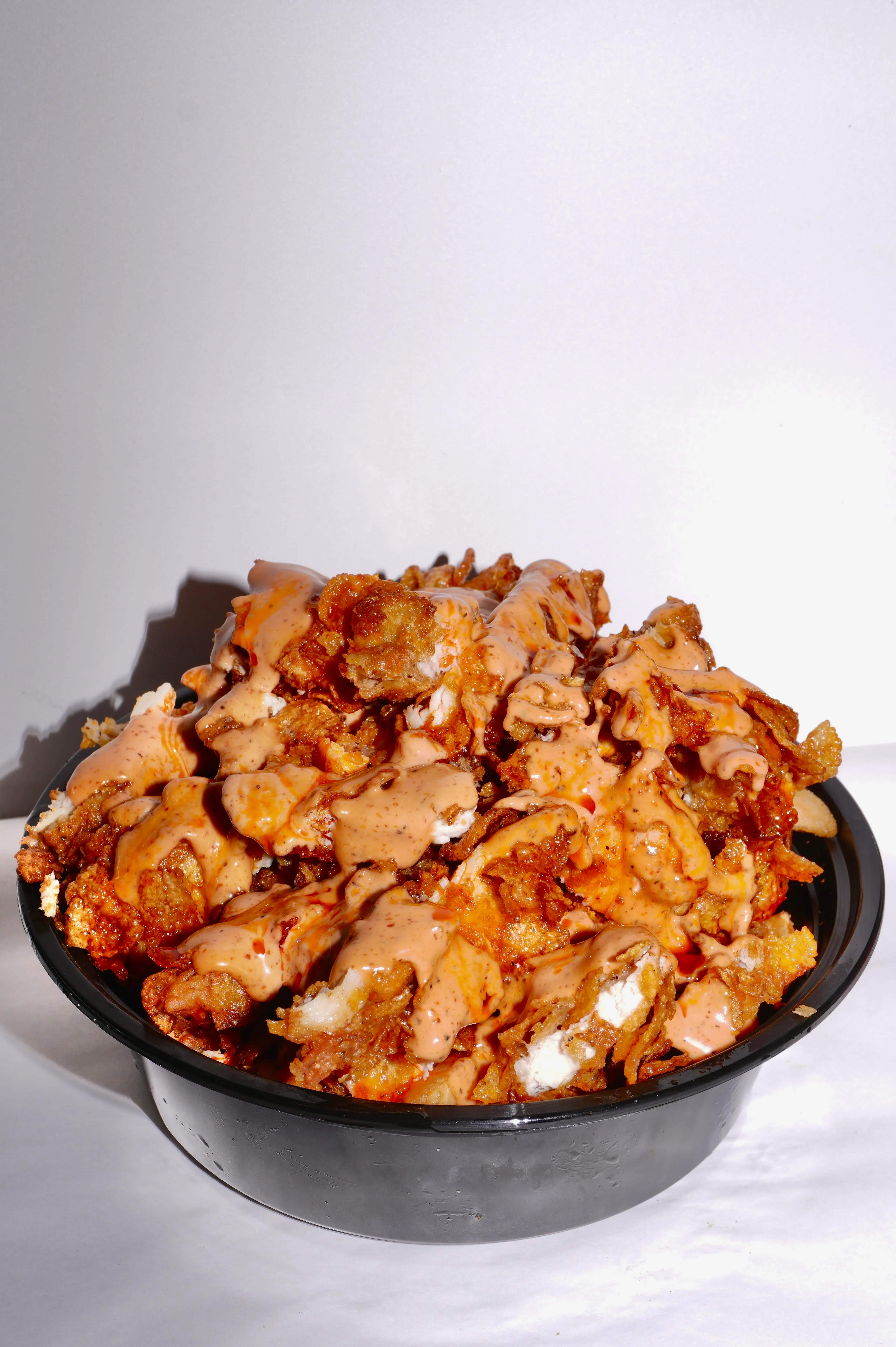 A large bowl overflowing with fried snacks drizzled with a creamy sauce, showcasing a mix of textures and colors.