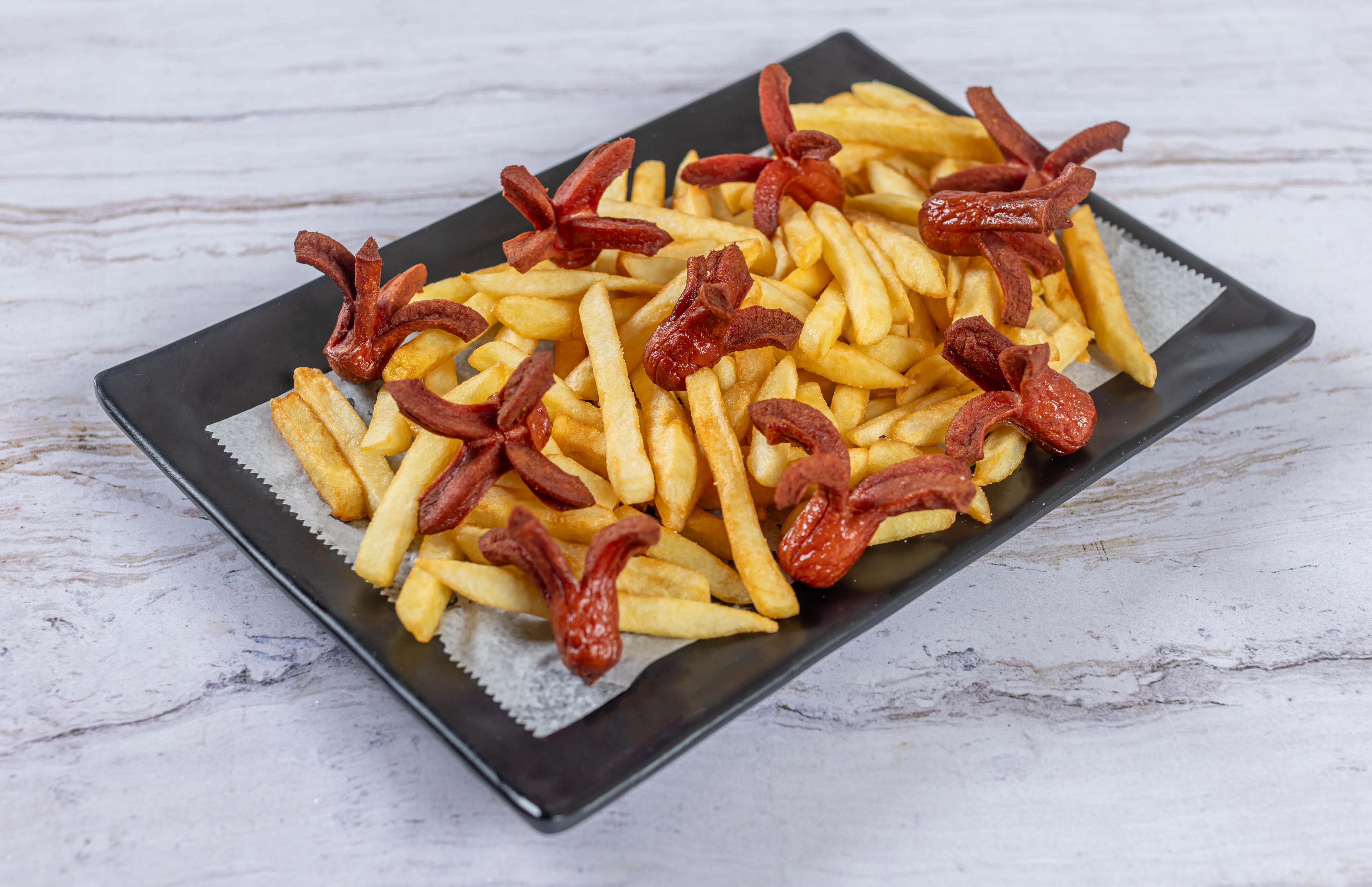 A fun kids' meal from El Budare Cafe, featuring french fries topped with fried hot dogs cut into playful octopus shapes.