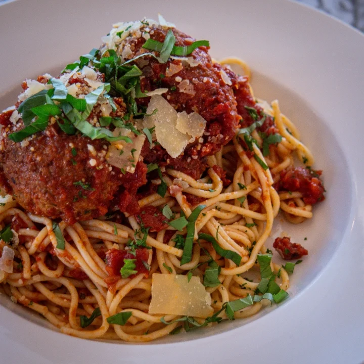 A bowl of spaghetti topped with meatballs, rich tomato sauce, and garnished with herbs and cheese.