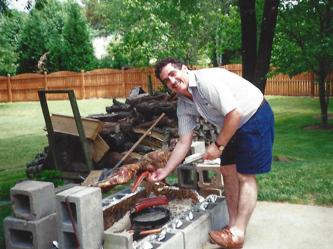 Man grilling a whole lamb outdoors in a backyard setting