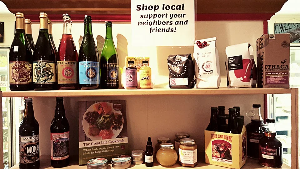A shelf filled with various local products, including beverages and packaged goods, with a sign encouraging support for local businesses.