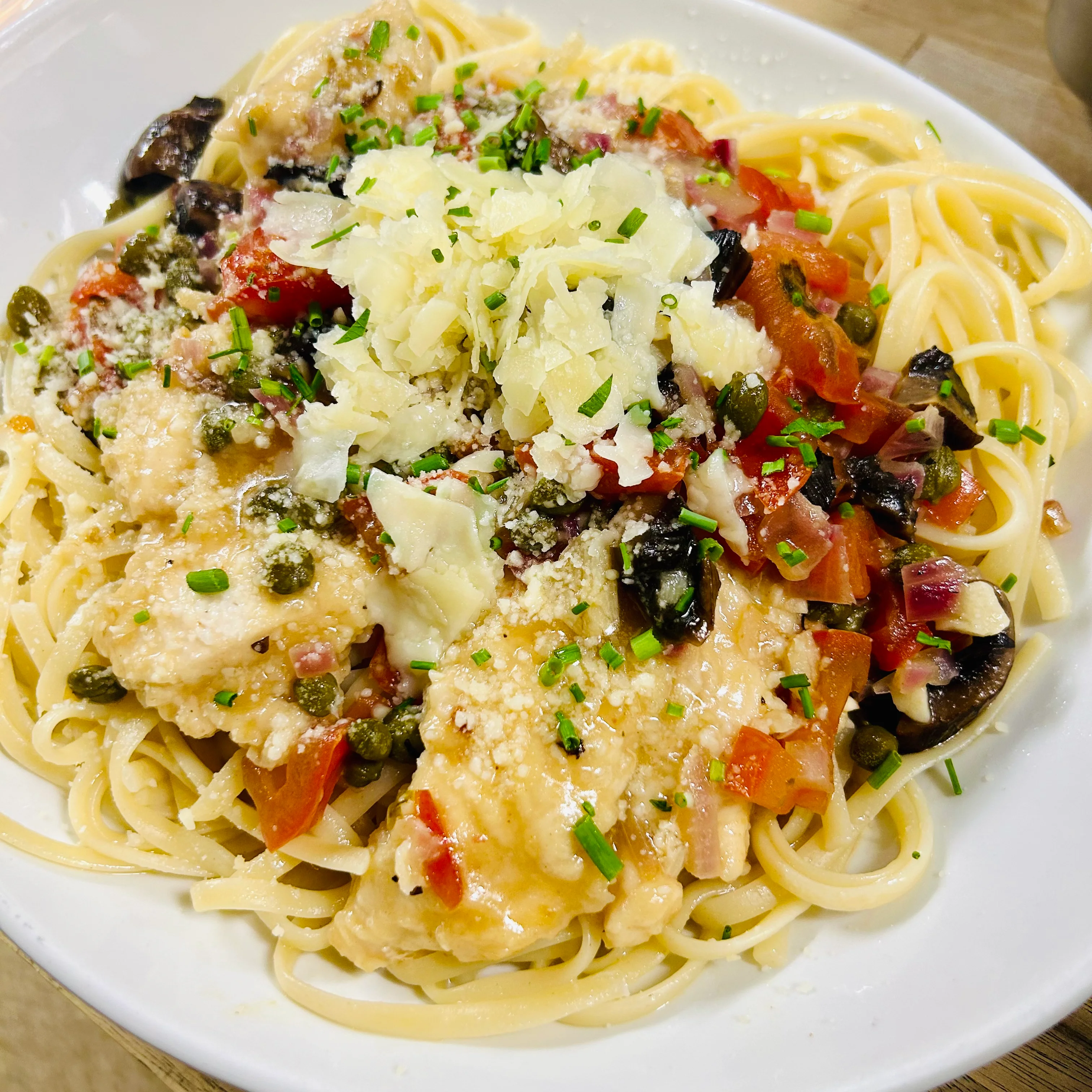 A plate of spaghetti topped with herbs, cheese, diced tomatoes, and olives, garnished with green chives.
