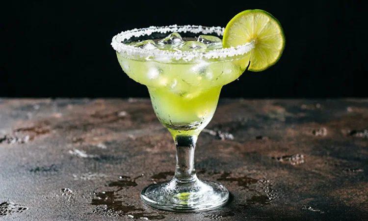 A refreshing green cocktail served in a margarita glass, garnished with a lime wedge and a salted rim.