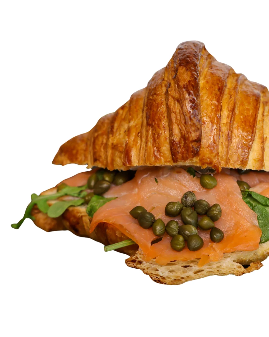 A croissant sandwich filled with smoked salmon, spinach, and capers, showcasing a flaky and golden pastry.