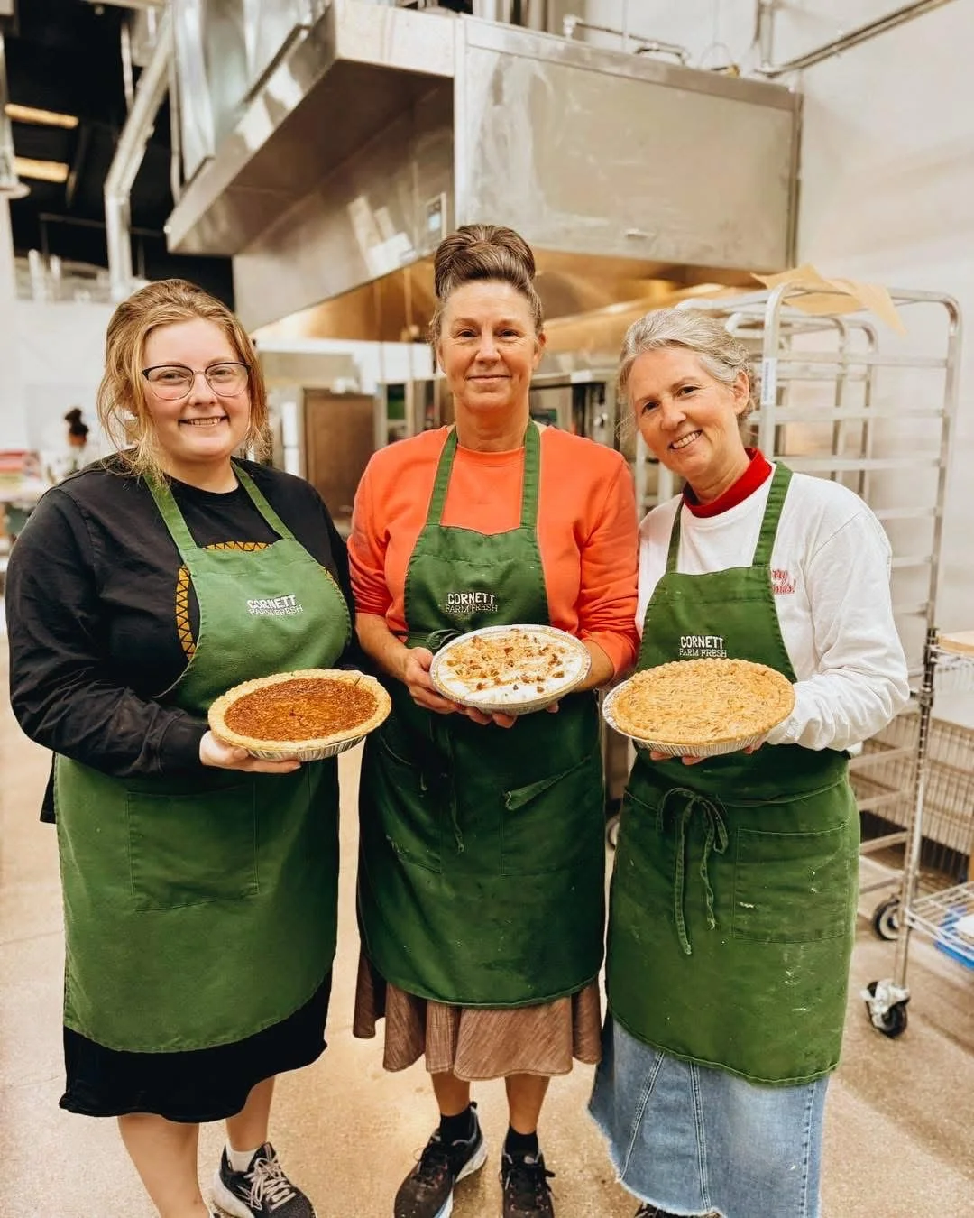 Three bakers showcasing homemade pies in a kitchen