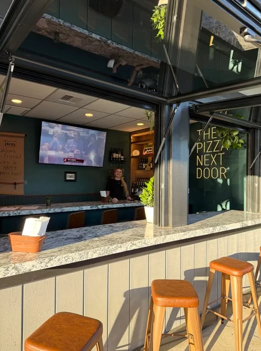 Bright pizzeria interior with bar seating and window lettering
