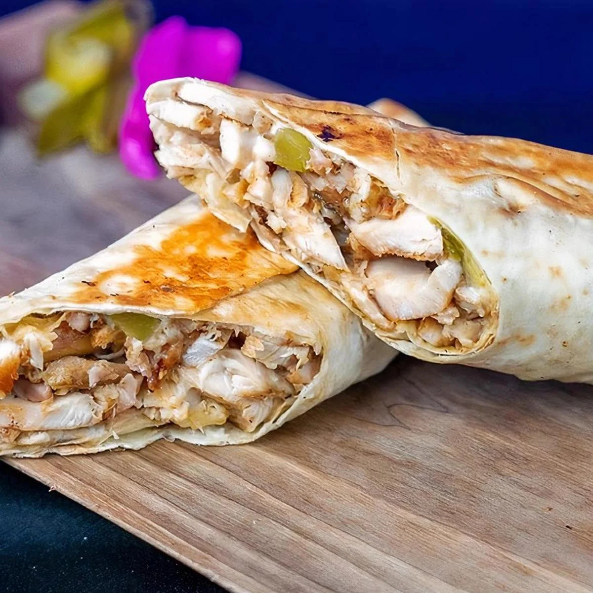Two halves of a grilled chicken wrap, showing the tender meat and vegetables inside. The wrap is golden and toasted, placed on a wooden surface.