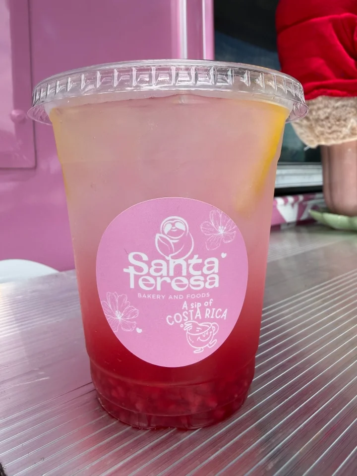 A refreshing drink in a clear cup with a pink label. The drink has layers of vibrant colors, indicating a mix of flavors, and is garnished with lemon slices.