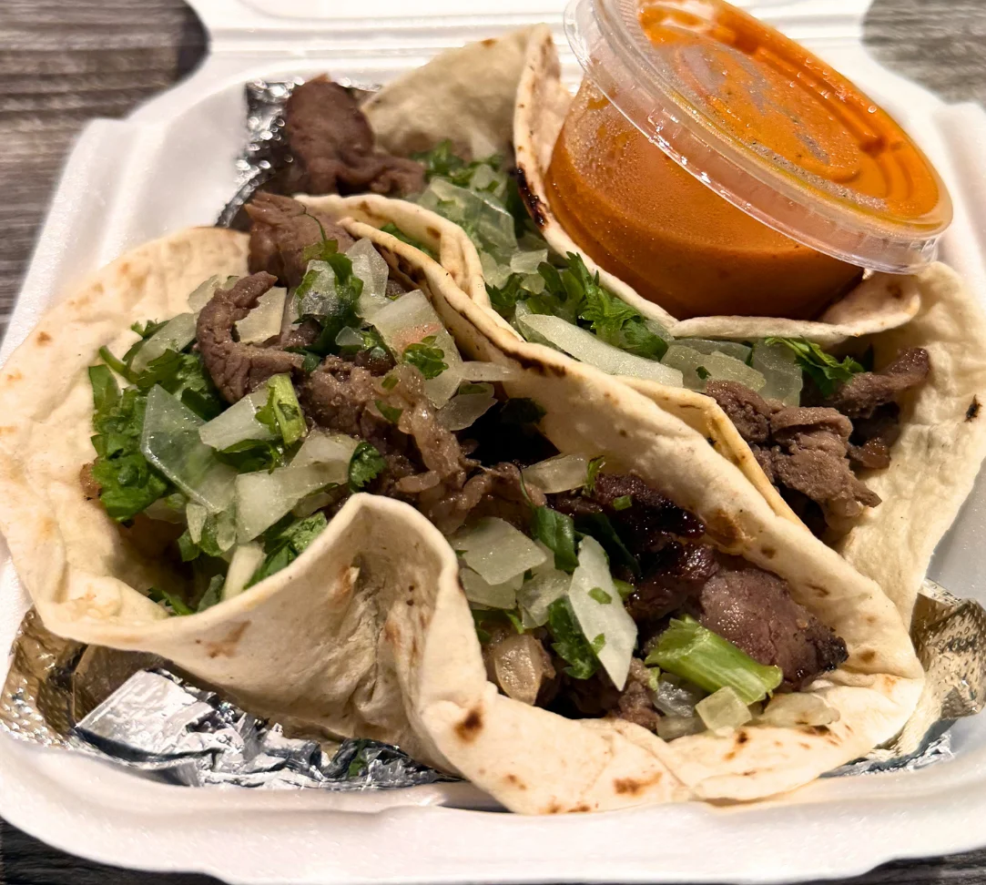 Two tacos filled with beef, onions, cilantro, and a side of sauce.