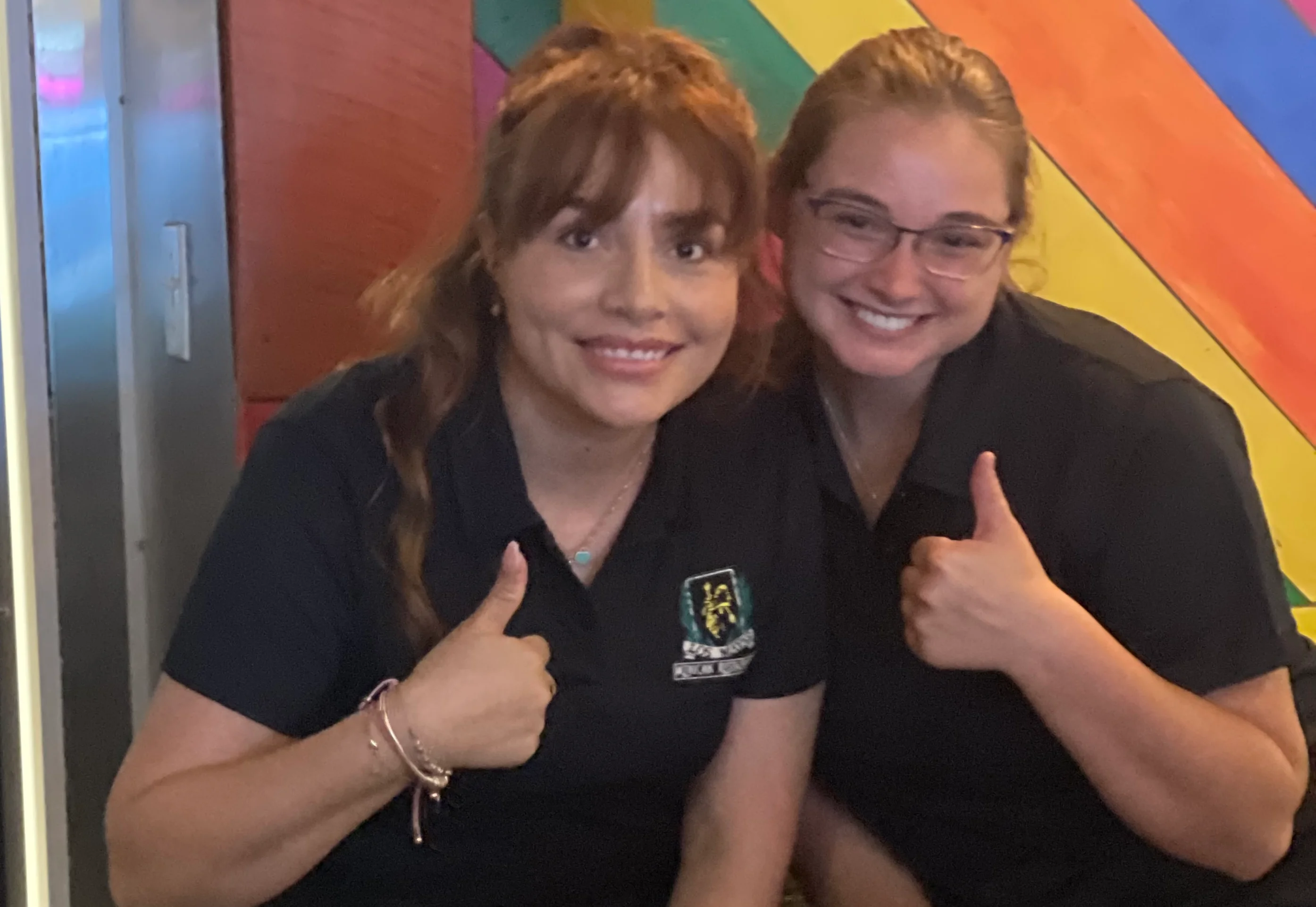 Two smiling restaurant staff giving thumbs up in a colorful setting