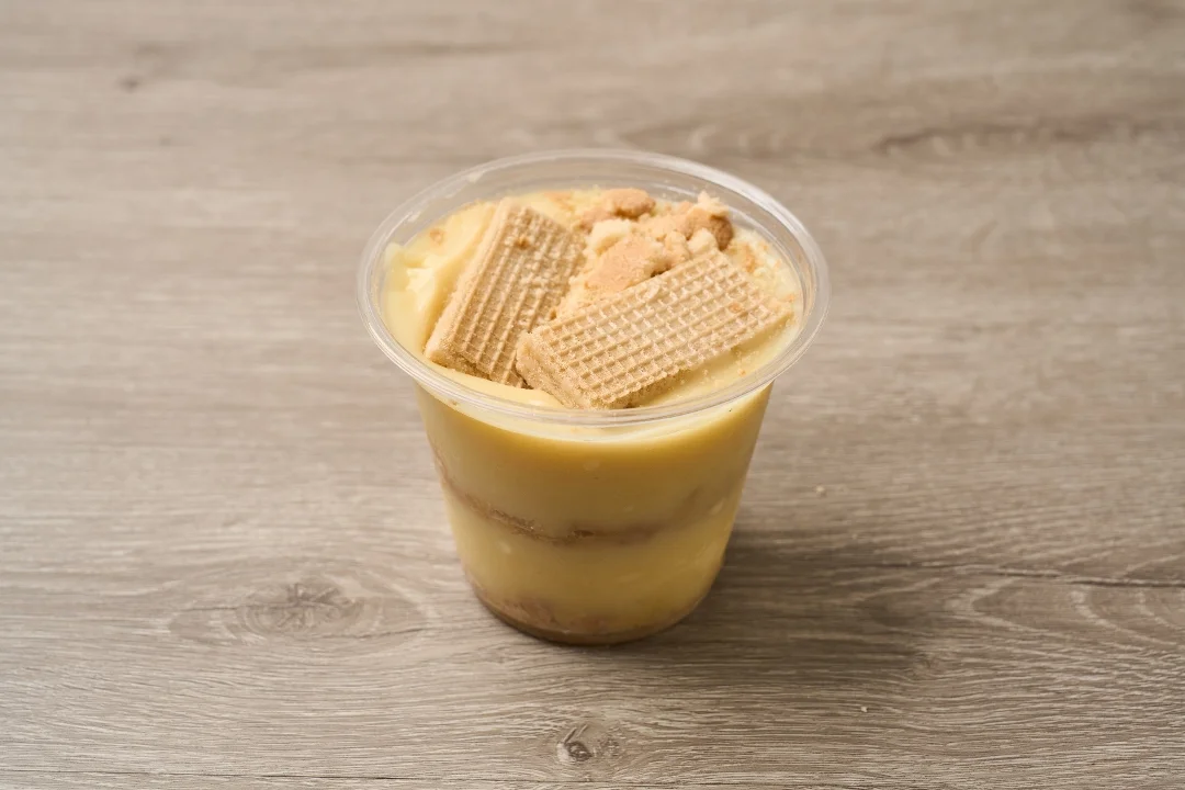 A dessert cup filled with creamy pudding topped with wafers and crushed cookies. The distinct layers of pudding and crumbs are visible.