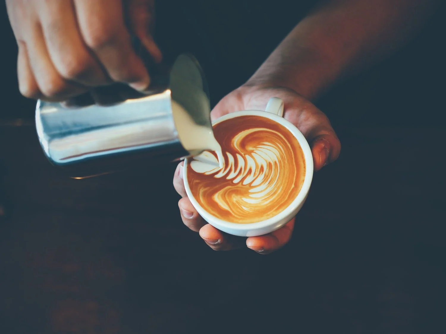 Barista pouring latte art into a white cup