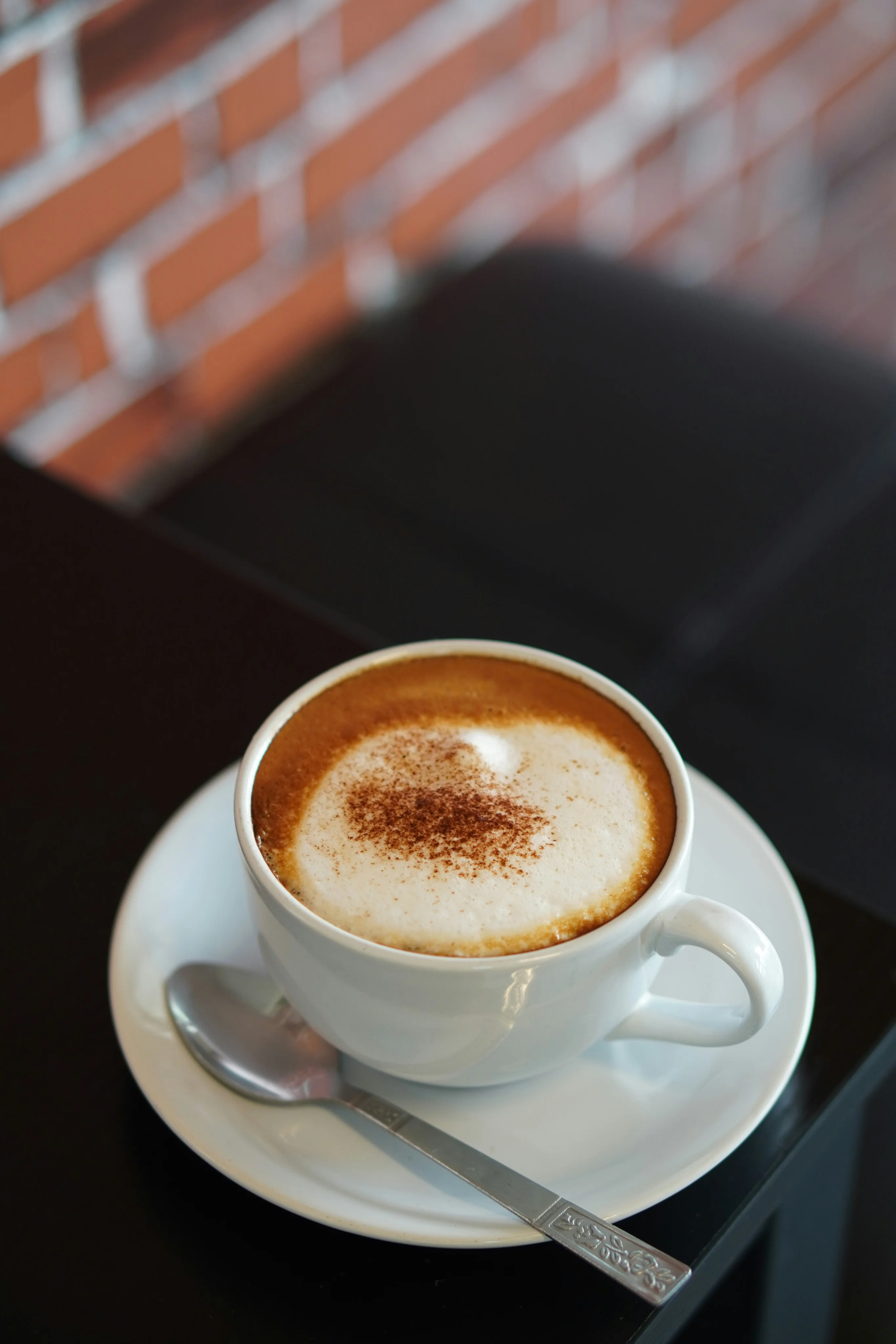 A cup of cappuccino with a foamy top, placed on a saucer with a spoon next to it.
